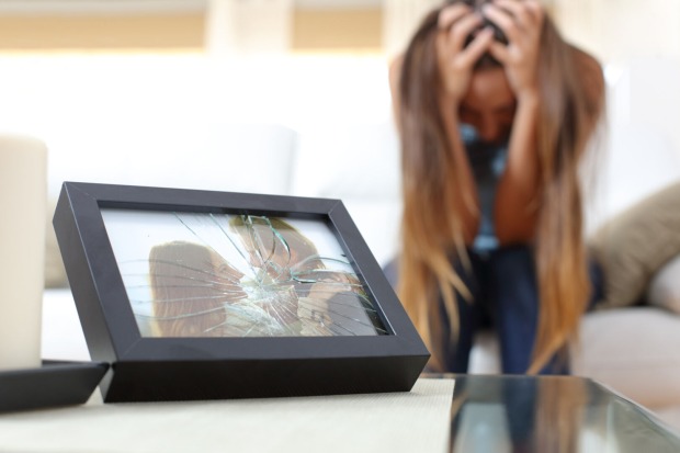 Eine verzweifelte Frau sitzt vor einem zersplitterten Foto von sich und ihrem Partner.