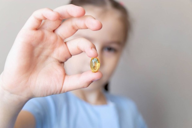 Junges Mädchen hält eine Vitaminkapsel zwischen den Zeigefinger und Daumen