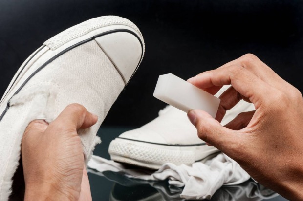 Weiße Sportschuhe werden mit einem Putzschwamm gereinigt.