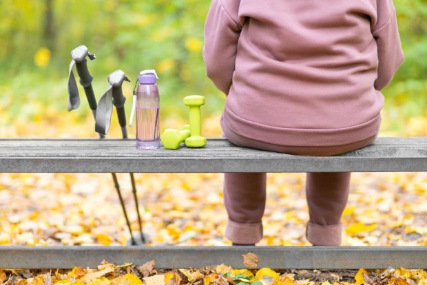 Rückansicht eines Menschen, der nach dem Sport auf einer Bank im Wald sitzt.