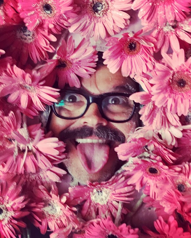Ein Mann mit Brille schaut zwischen pinken Blumen hervor