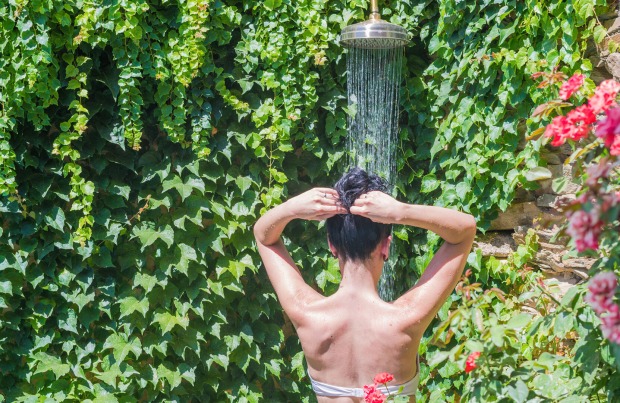 Frau steht unter einer Gartendusche | Credit: iStock.com/Diego Cerro Jimenez
