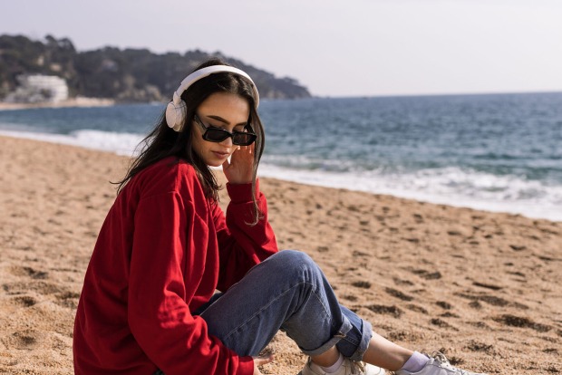Frau sitzt mit Kopfhörern am Strand | Credit: iStock.com/Alina Rosanova