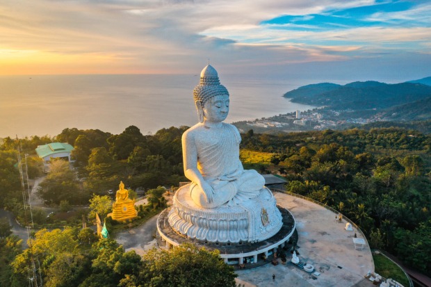 Eine Buddha-Statue auf einem Hügel, dahinter der Sonnenuntergang und das Meer