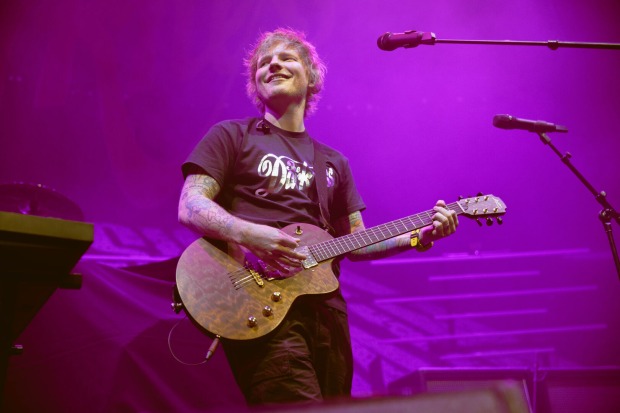 Ed Sheeran, der auf einer in violettes Licht getauchten Bühne Gitarre spielt