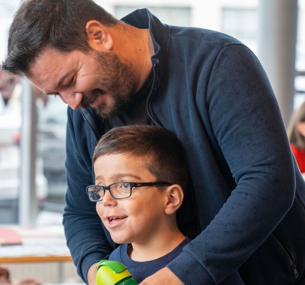 Mann beugt sich zu Kind hinunter, beide lachen