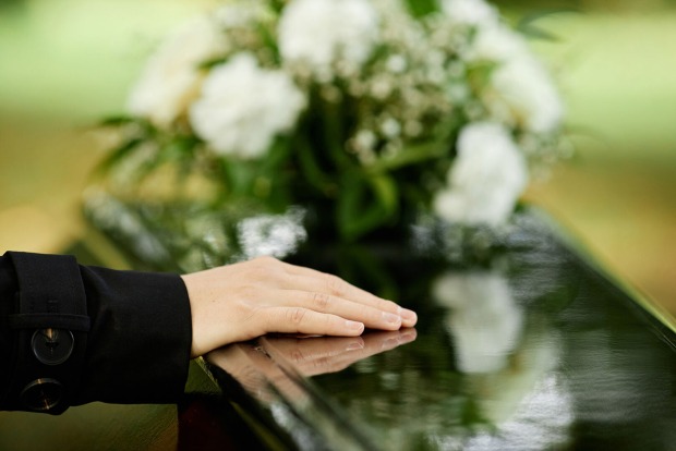 Trauernde Frau legt ihre Hand auf den schwarzen Sarg | Credit: iStock.com/SeventyFour