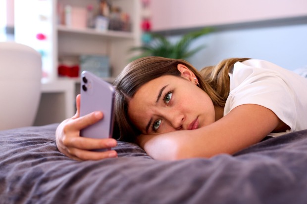 Ein Mädchen liegt mit ihrem Handy auf dem Bett.