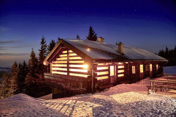 Eine beleuchtete Almhütte umgeben von Schnee