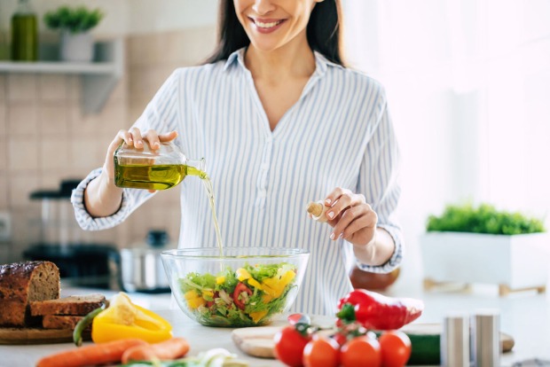 Frau gibt Olivenöl in den Salat | Credit: iStock.com/Povozniuk