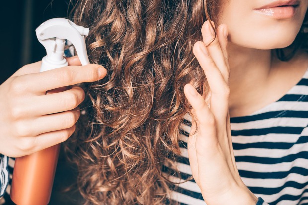 Frau sprüht ihre gelockten Haare mit einem Pflegespray ein | Credit: iStock.com/iprogressman