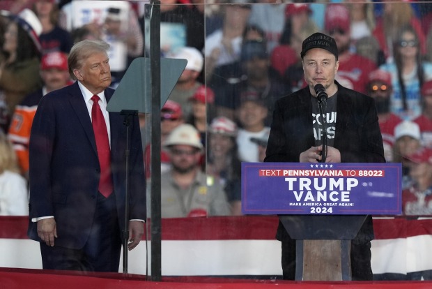 Elon Musk, der hinter einem Rednerpult auf einer Wahlkampfveranstaltung Donald Trumps steht