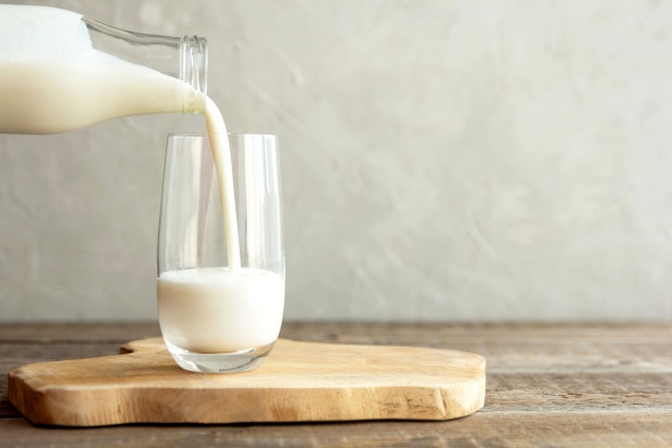 Ein Glas, in das aus einer Flasche Milch gegossen wird