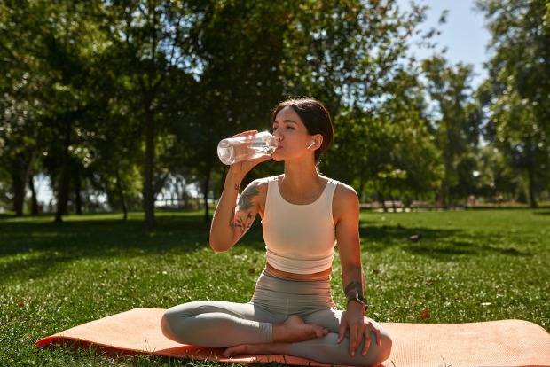 Frau sitzt auf Yoga-Matte und trinkt Wasser | Credit: iStock.com/LanaStock