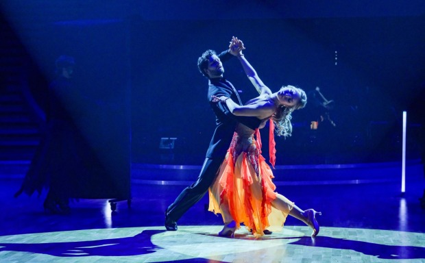 Aaron Karl und Katya Mizera tanzen im Finale von Dancing Stars 2025 eine dramatische Hebefigur im Scheinwerferlicht. Sie trägt ein orange-rotes Kleid, er einen schwarzen Anzug.