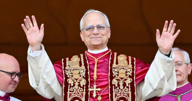 Papst Leo XIV. steht in päpstlicher liturgischer Kleidung auf dem Balkon des Petersdoms und hebt beide Hände zum Gruß. Links und rechts neben ihm stehen Kirchenvertreter.