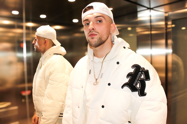 Rapper Gavis Dean, der in einem Fahrstuhl steht und eine weiße Baseball-Kappe, einen weißen Kapuzenpullover sowie eine weiße Sportjacke trägt