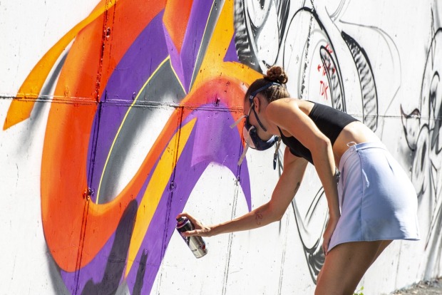 Ein Mädchen malt ein buntes Graffiti an die Wand.