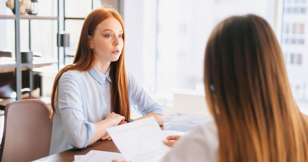 Frau im Vorstellungsgespräch, sitzt gegenüber einer Person mit Unterlagen in einem hellen Büro.