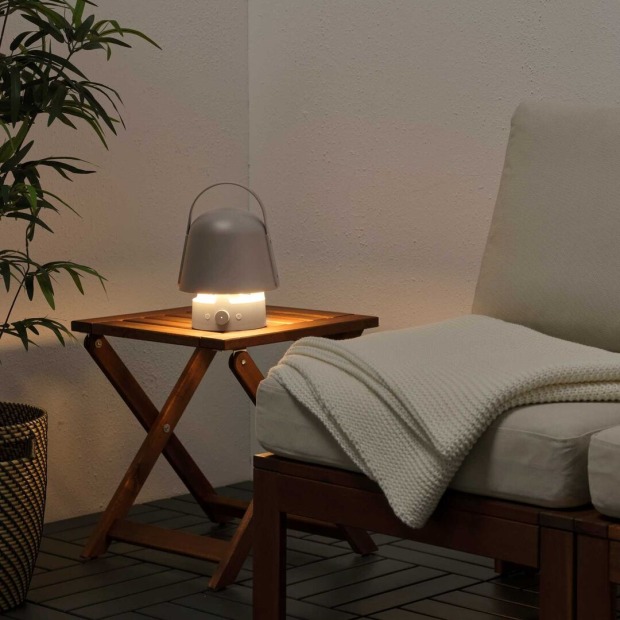 Gemütliche Sitzecke mit Holzstuhl, Decke und kleiner Tischleuchte in sanftem Licht – tragbare Lampe mit Lautsprecherfunktion sorgt für stimmungsvolle Atmosphäre.