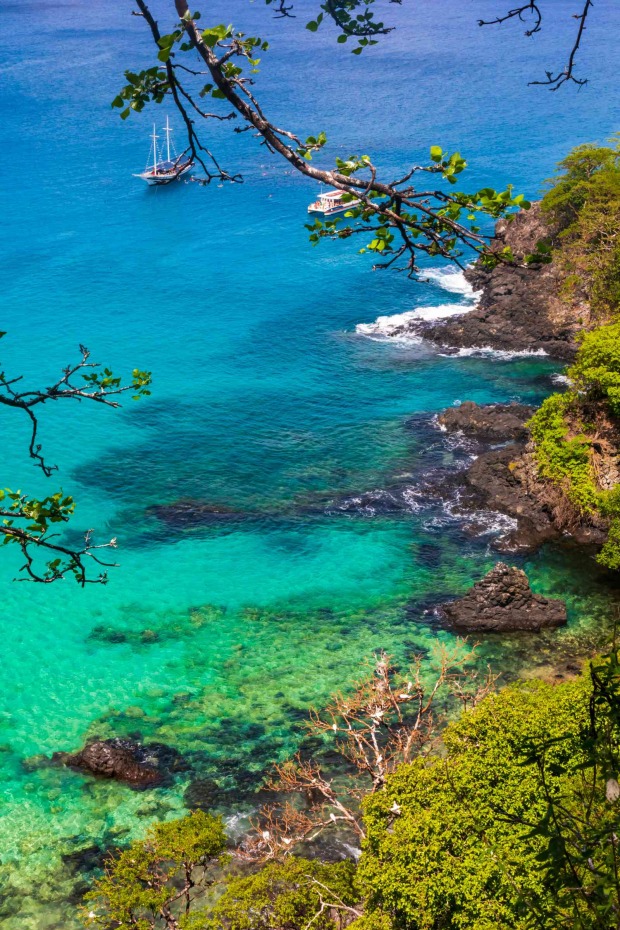 Baía do Sancho in Brasilien mit türkisfarbener Bucht, goldenem Sandstrand und bewachsenen Klippen aus der Vogelperspektive.