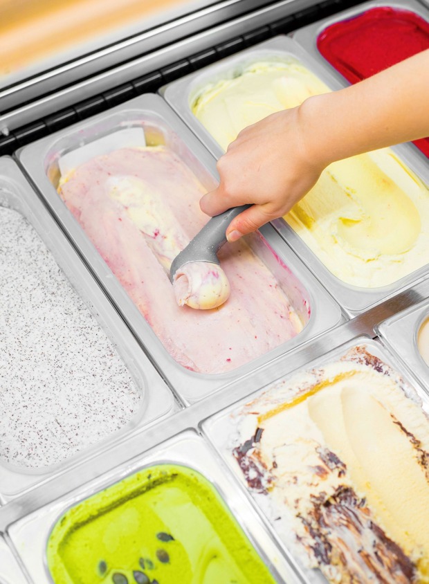 Hand eines Eisverkäufers, der mit einem Eisportionierer das Eis aufrollt