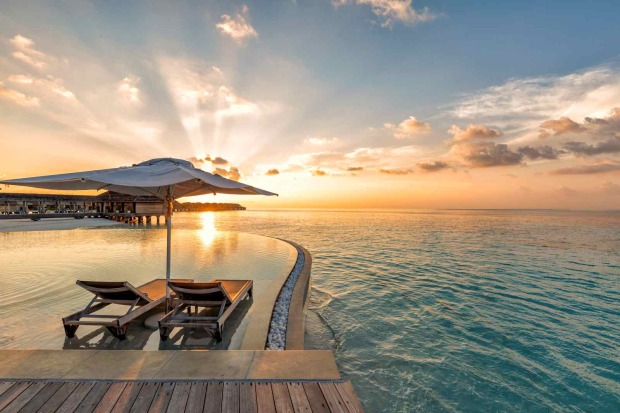 Liegestühle am Pool mit Blick auf das Meer bei Sonnenuntergang auf den Malediven