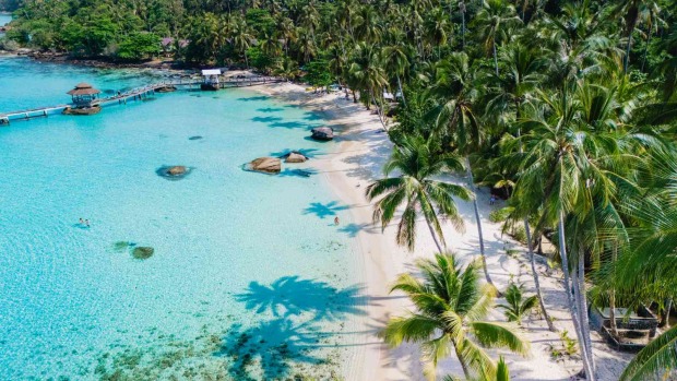 Tropischer Strand auf Koh Kood mit Palmen, hellem Sand, türkisfarbenem Wasser und einem Holzsteg mit Pavillon.