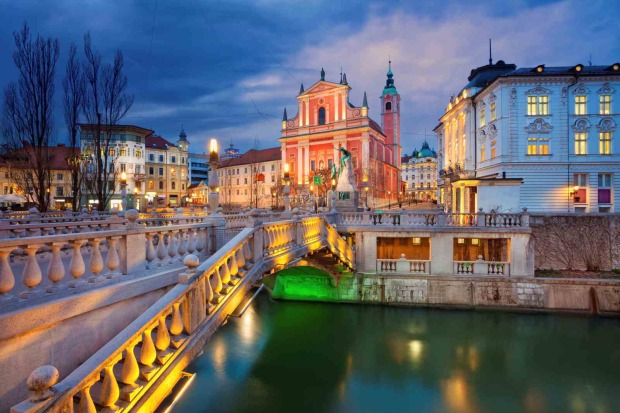 Beleuchtete Altstadt von Ljubljana mit Brücke und Kirche am Fluss bei Abenddämmerung