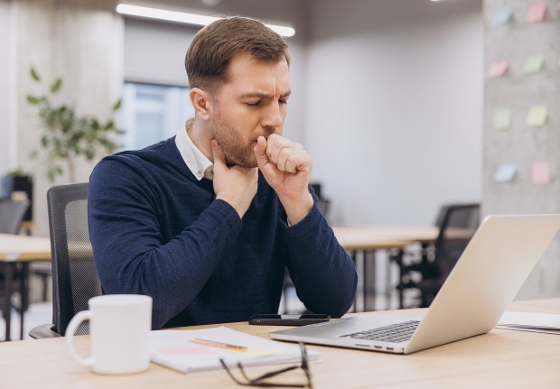 Mann räuspert sich bei der Arbeit am Laptop im Office | Credit: Anatoliy Cherkas/Shutterstock