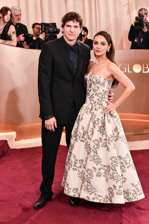 Ashton Kutcher im schwarzen Anzug neben Mila Kunis im trägerlosen Abendkleid auf einem roten Teppich.