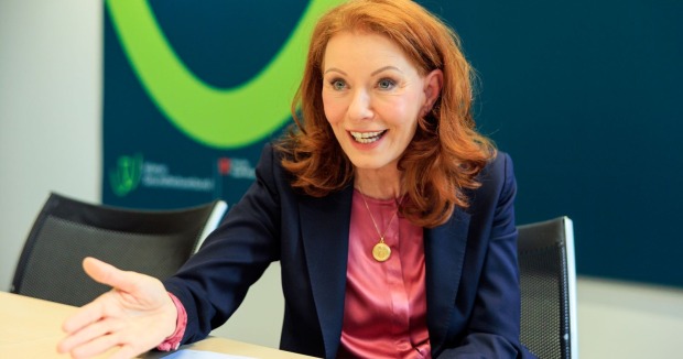 Frau  mit roten Haaren, weinroter Bluse und blauem Blazer sitzt am Tisch