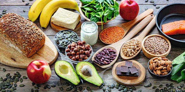 Magnesiumreiche Lebensmittel wie Nüsse, Samen, Avocado, Bananen, Vollkornbrot, Hülsenfrüchte und Lachs auf Holztisch