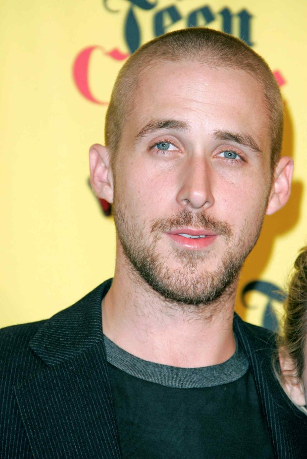 Junger Ryan Gosling mit raspelkurzen Haaren und leichtem Bart bei einem Event vor gelbem Hintergrund.