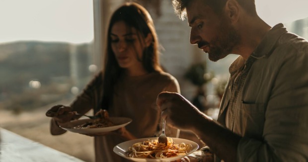 Zwei Menschen essen gemeinsam Pasta in warmer Abendstimmung. Die Szene wirkt ruhig, gemütlich und intim.