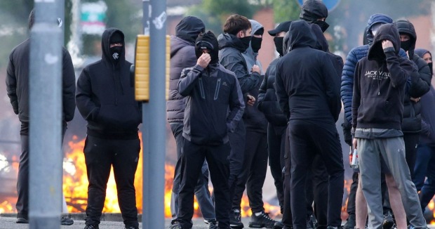 Vermummte Männer bei Ausschreitungen in Belfast vor Feuer und Barrikaden auf der Straße