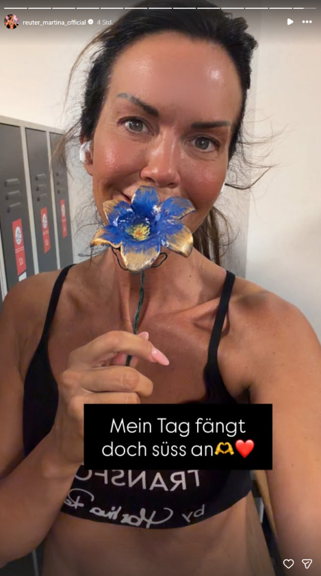 Martina Reuter hält nach dem Training im Fitnessstudio eine blaue Blume in der Hand und lächelt für ein Selfie. Die ORF-Moderatorin freut sich über die Überraschung eines Fans im Gym.