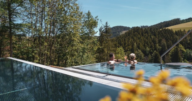 Ein Paar im Outdoor-Pool vor einem Hotel mit Blick auf die Almen | Credit: Hotel Königswieserhof