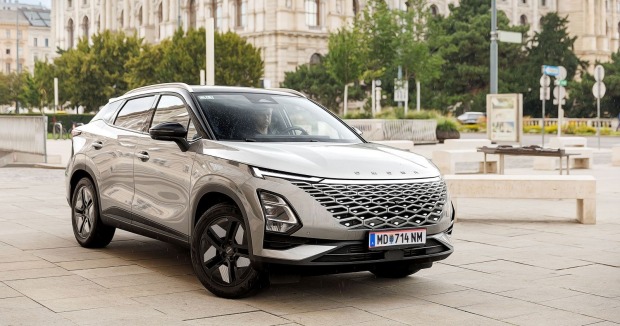 Ein silberner Hybrid-SUV Omoda 5 parkt in einer Stadt. Zu sehen sind historische Gebäude - vermutlich ist man in Wien.