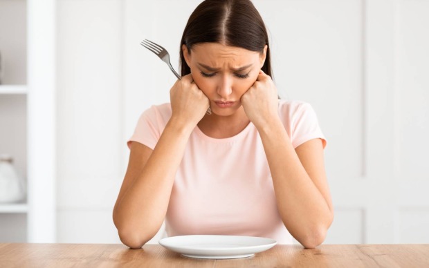 Frau sitzt hungrig vor einem leerem Teller | Credit: Prostock-studio/Shutterstock