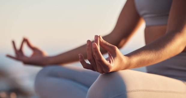 Frau bei Mediation, Strand, Sonnenuntergang | Credit: PeopleImages/Shutterstock