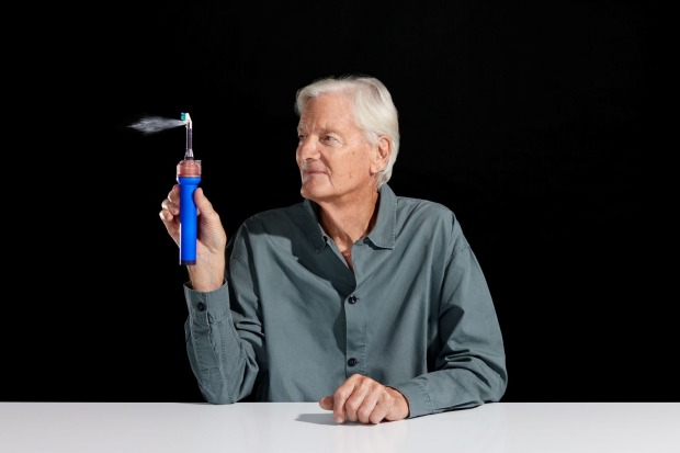 James Dyson hält die Dyson Zahnbürste CameraJet mit aktiviertem Mundspülungsstrahl in der Hand.