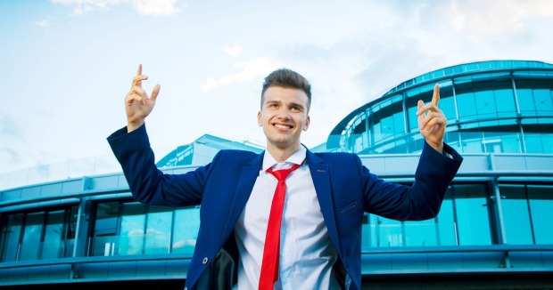 Mann im blauen Anzug und mit roter Krawatte steht vor einem modernen Gebäude und zeigt nach oben.