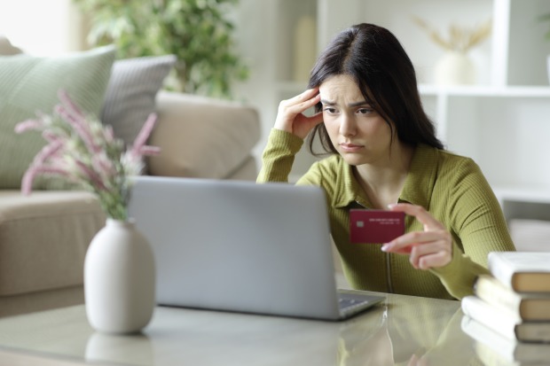 Eine junge Frau blickt mit einem besorgten Gesichtsausdruck auf ihren Laptop und hält eine Kreditkarte in einer Hand