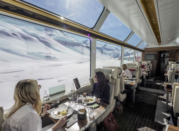 Fahrgäste sitzen an gedeckten Tischen in der Excellence Class des Glacier Express.