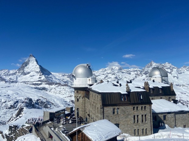 Das Kulmhotel Gornergrat mit seiner Sternwarte steht in verschneiter Hochgebirgslandschaft, dahinter ist das Matterhorn zu sehen