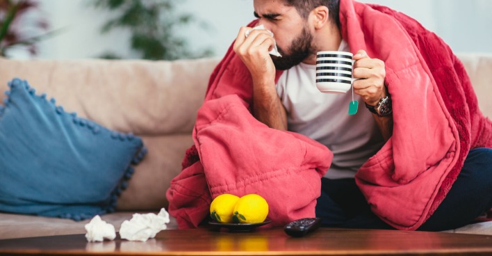 Mann kuriert Erkältung auf Sofa mit Hausmitteln