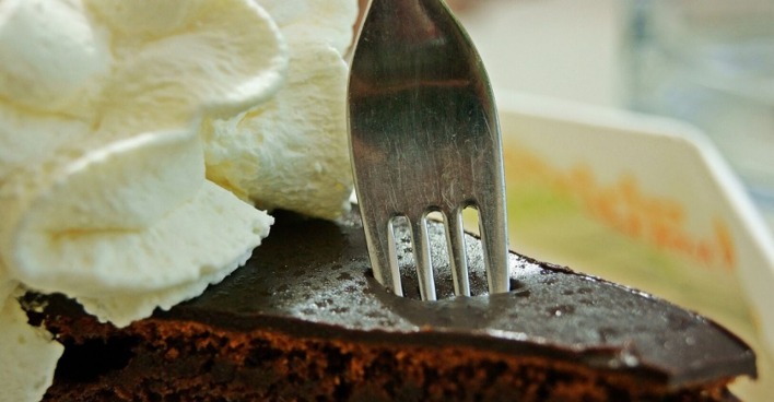 Eine Gabel sticht in eine Sacher-Torte mit Schlagobers