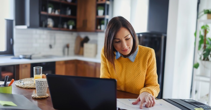 Eine Frau arbeitet auf ihrem Küchentisch vor ihrem Laptop