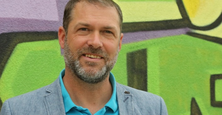 Stadtrat Markus Geiger steht vor einer mit Graffiti bemalten Wand.